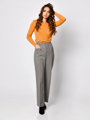 Young beautiful brunette woman posing in new casual orange blouse sweater and grey pants