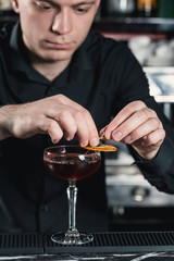 bartender making Boulevardier Cocktail Finishing cocktail putting orange slice on top. Bar on a background