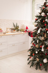 Interior light kitchen and red christmas decor. Preparing holiday dinner at home on the kitchen concept. Decorated new Year fir. Selective focus