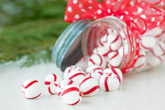 Photograph of red and white Christmas peppermints following out of a jar with Christmas greenery