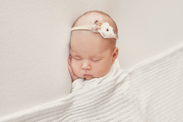 Cute newborn baby girl lies swaddled in a white blanket. Baby goods packaging template. Closeup portrait of newborn baby with smile on face. Healthy and medical concept. 