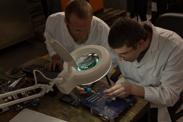 Robotics engineers assembling circuit board at desk