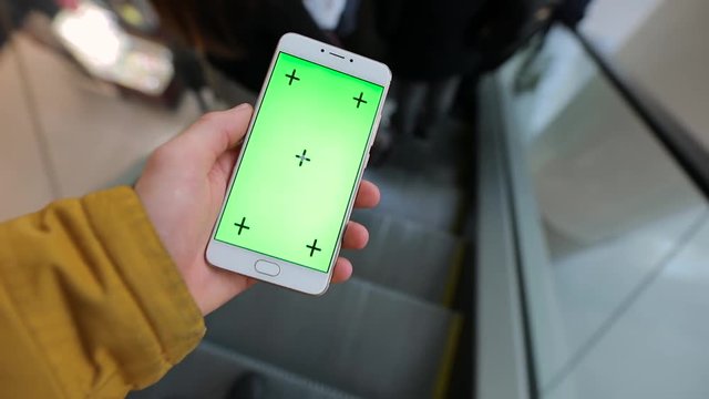 Male hand using smartphone with green screen in the escalator of shopping mall