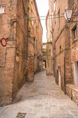 Fototapeta na wymiar Seitenstraße Pflastersteine mit Ziegelhäuser in der Altstadt von Siena Italien