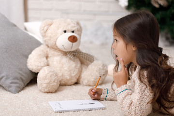 Cute child girl writing letter to Santa Claus at home