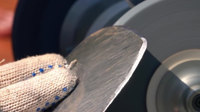 Sharpening of worn garden tool with unbalanced grinding machine in slow motion close up. Handicraft scene with fingers in safety glove, round-pointed steel shovel and turning grindstone wheel.