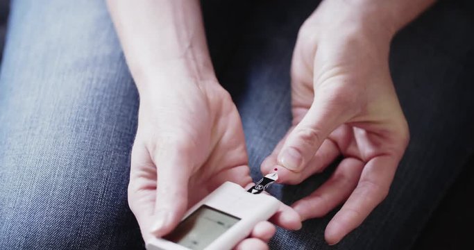 Blood sugar, diabetes and healthcare concept - a woman takes a blood sample with a lancet and measures blood sugar levels with a glucose meter at home.