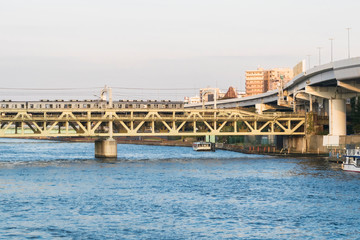 Details of modern urban infrastructure illustrating mass transit concept featuring railway bridge across river with metro train and elevated highway in Tokyo Japan. November 2018.