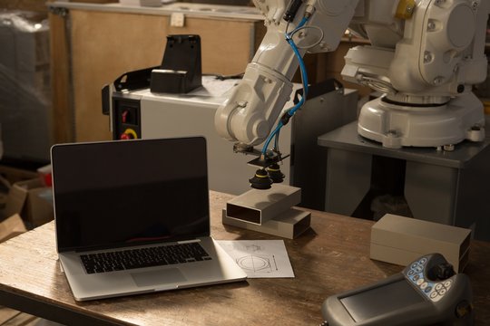 Laptop, robotic machine and remote control on table