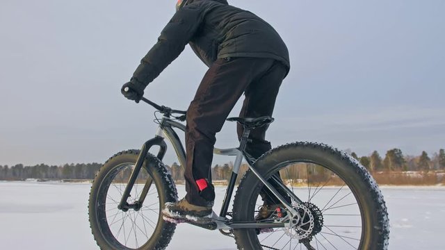 Professional extreme sportsman biker riding fat bike in outdoors. Cyclist ride in winter on snow ice. Man does trick on mountain bicycle with big tire in helmet and glasses. Slow motion in 180fps.