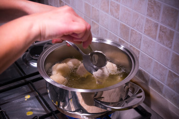 Woman's hands that make the Dough Slip from a Spoon into the Pot during the Preparation of an Italian Christmas Traditional Dish called Pettole