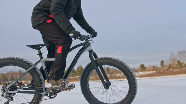 Professional extreme sportsman biker riding fat bike in outdoors. Cyclist ride in winter on snow ice. Man does trick on mountain bicycle with big tire in helmet and glasses. Slow motion in 180fps.