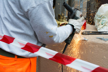 Fototapeta premium Worker using an Orbital Grinder on Steel Surface wearing Orange Work Trousers