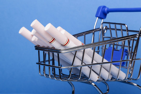 Smoking concept. Cigarettes in shopping cart, shopping trolley on blue background