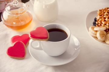 Coffee and a heart shaped cookies, honey, milk and waffles