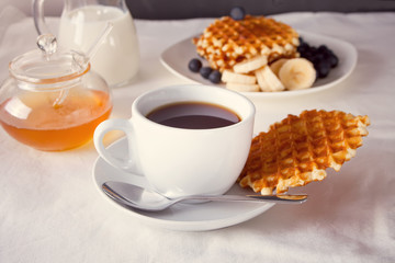 Cup of coffee and waffles with bananas, blueberries and honey.