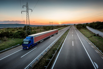 Obraz na płótnie Canvas Very long lorry truck on the highway road through the countryside at sunset