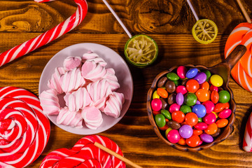 Ceramic plate with marshmallow, candy cane and lollipops on a wooden table. Top view