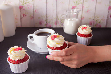 Cup of coffee and cupcakes with hearts on the wooden table. Woman holding cupcake.
