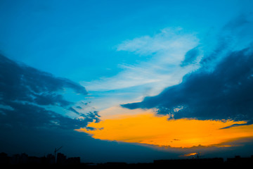 Naklejka premium Atmospheric blue cloudy sky behind silhouettes of city buildings. Cobalt and orange background of sunrise with dense clouds and bright yellow sunny light for copy space. Cyan heaven above clouds.