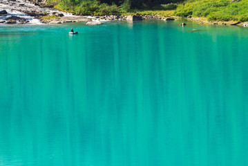 View above fisherman in boat on azure water of mountain lake. Fishing on highlands. Mountainside with rich vegetation in sunlight. Atmospheric minimalist beautiful landscape of nature in sunny day