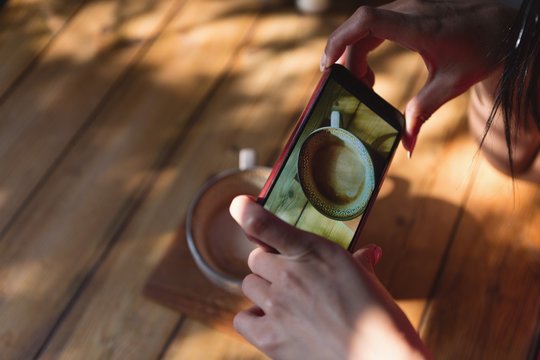 Woman taking picture of coffee cup in cafe