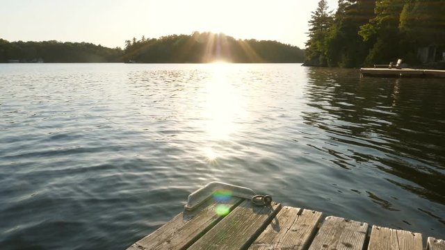 Slow motion shot of freshwater lake and sunshine with dock and cottages. Cottage country in Ontario, Canada.