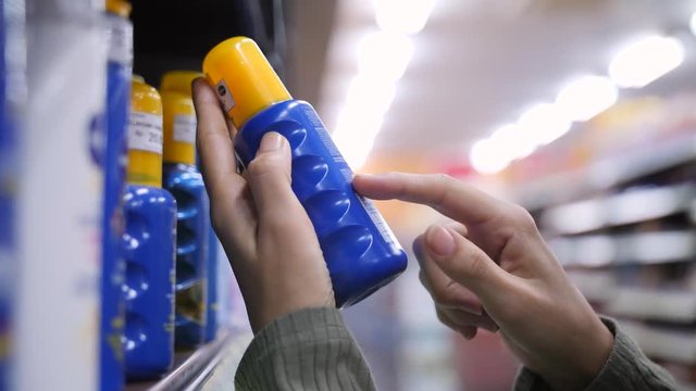 Young Woman Choosing Sunscreen Cream and Reading Ingredients On Bottle in Body Care Cosmetics Store. 4K Slowmotion.