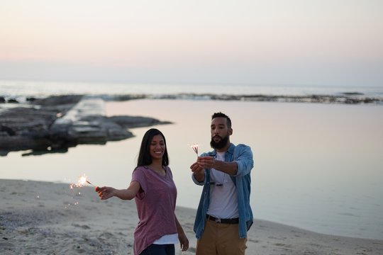 Smiling couple holding sparkler on beach