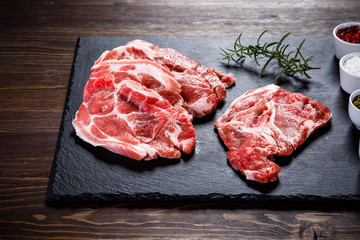 Raw beefsteaks on black stone on wooden background