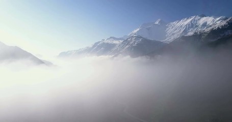 Aerial drone elevating pan above low clouds to reveal snow covered Himalayan Annapurna mountain range in early morning at high altitude above Manang valley landscape in Nepal. 4k 1.9:1 23.976fps