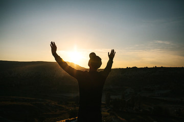 Fototapeta premium A man stands on top of a mountain in solitude, admires the beautiful view of the natural landscape and raises his hands up showing how he is free and happy.