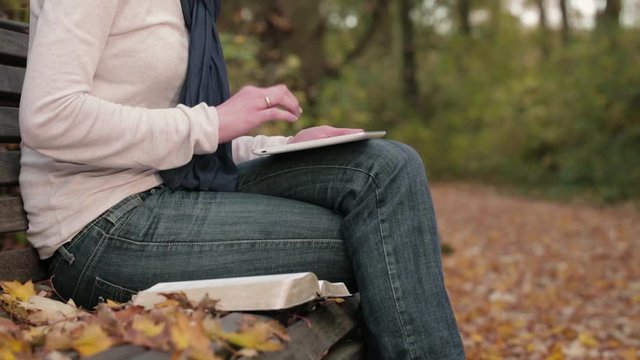 Woman studies the Bible in a park with the help of a tablet.