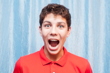 A teenager on a blue background is emotionally happy because he has braces on his teeth and his...