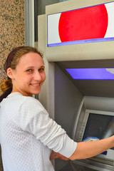 Fototapeta na wymiar A young and beautiful girl stands near the ATM, enters a PIN code and withdraws money from the card. The concept of finance and money.