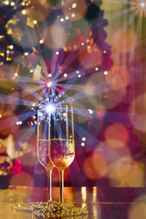 New Years Eve celebration background with pair of flute,candles glitter and defocused background, with christmas tree light forming a nice bokeh, holiday concept, frontal view,,copyspace