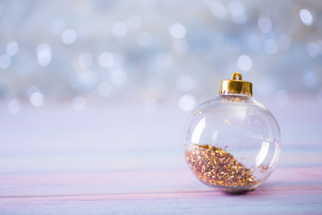 Glass transparent Christmas ball with gold tinsel inside on light bokeh background.