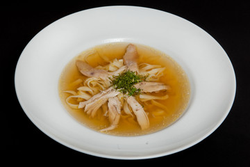 Chicken soup in a white plate on a black background