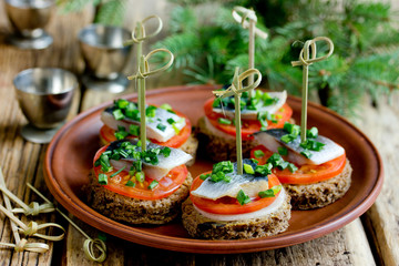 Canapes with rye bread, salted herring fillet, mustard, onion, tomato and skewers on plate