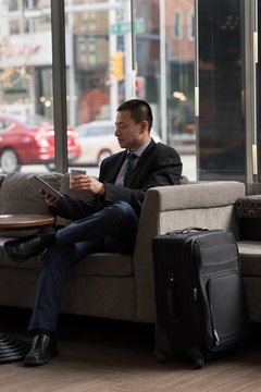 Businessman having whiskey while using digital tablet on sofa