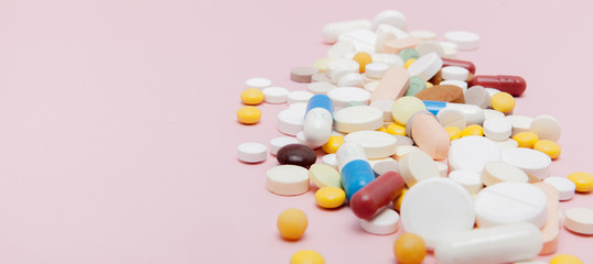 Colorful tablets with capsules on a pink background