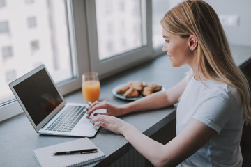 Side view of working lady in casual clothes with laptop in front of window. She looking at screen