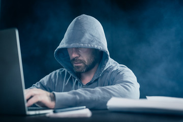 mysterious criminal bearded male hacker, doing something illegal on a laptop, in the dark