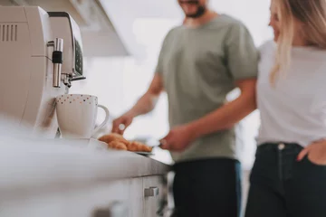 Poster Blurred portrait of man cooking breakfast for his woman. Focus on coffee mug with coffee maker © Yakobchuk Olena