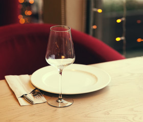 Served table in the restaurant. Empty wine glasses, a plate on the background of the bright lights of the Christmas garland.