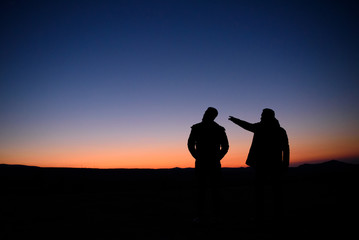 Silhouettes of two people at sunset on the horizon