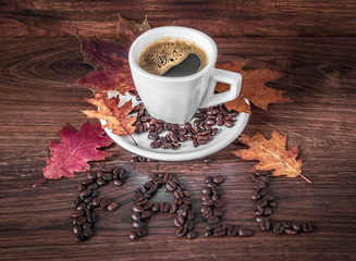 Morning cup of black coffee in an autumn setting. 'FALL' writing made of coffee beans on a wooden table.