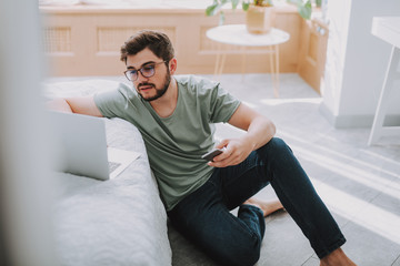 Bearded young man sitting on the floor while surfing the Internet