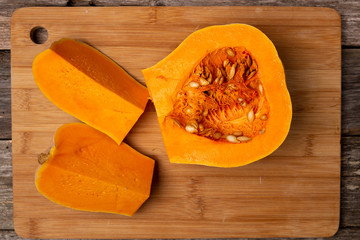 Sliced raw orange pumpkin on wooden cutting board