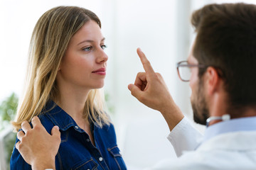 Attractive male doctor ophtalmologist checking the eye vision of beautiful young woman in modern...